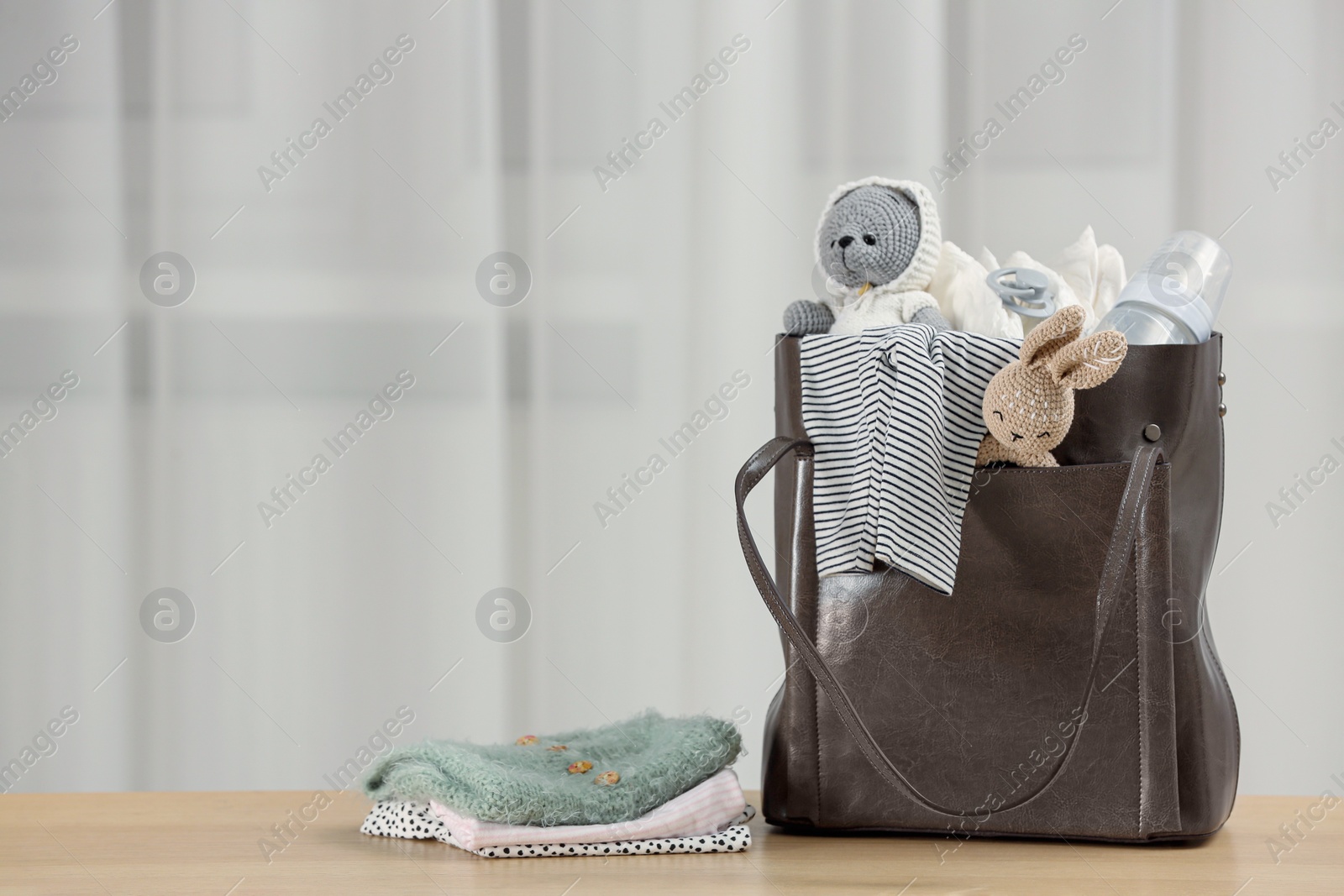 Photo of Mother's bag with baby's stuff on wooden table indoors. Space for text