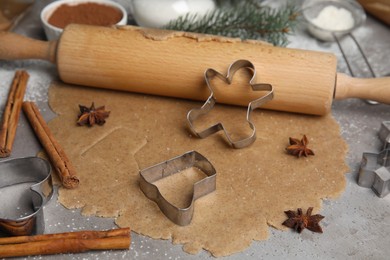 Homemade Christmas biscuits. Raw dough, rolling pin and cookie cutters on grey table, closeup