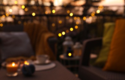 Blurred view of garden furniture with pillow, soft blanket and burning candles at balcony