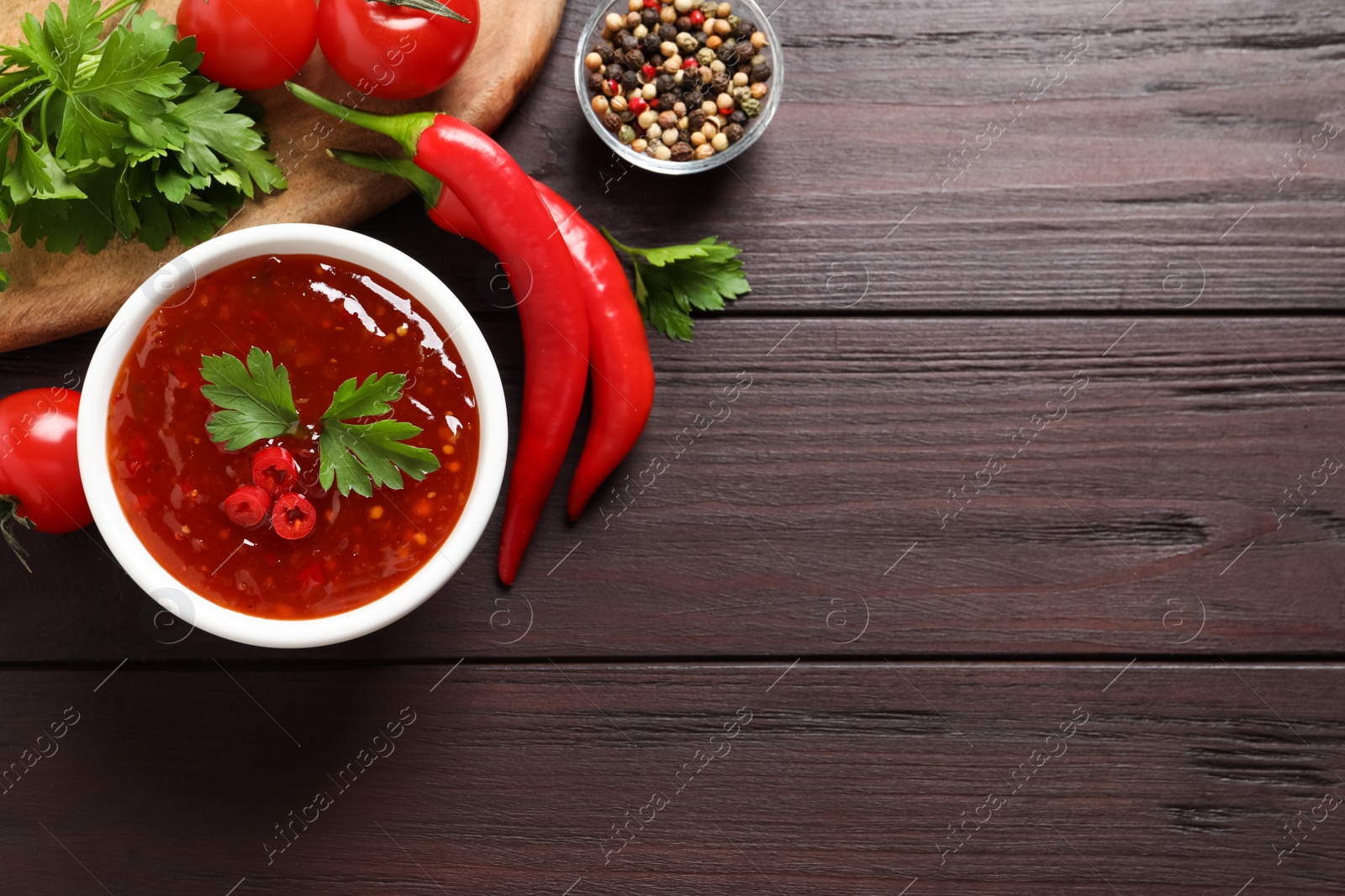 Photo of Spicy chili sauce and ingredients on wooden table, flat lay. Space for text