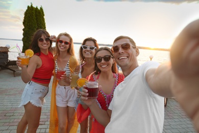 Photo of Happy people with refreshing drinks taking selfie at party outdoors
