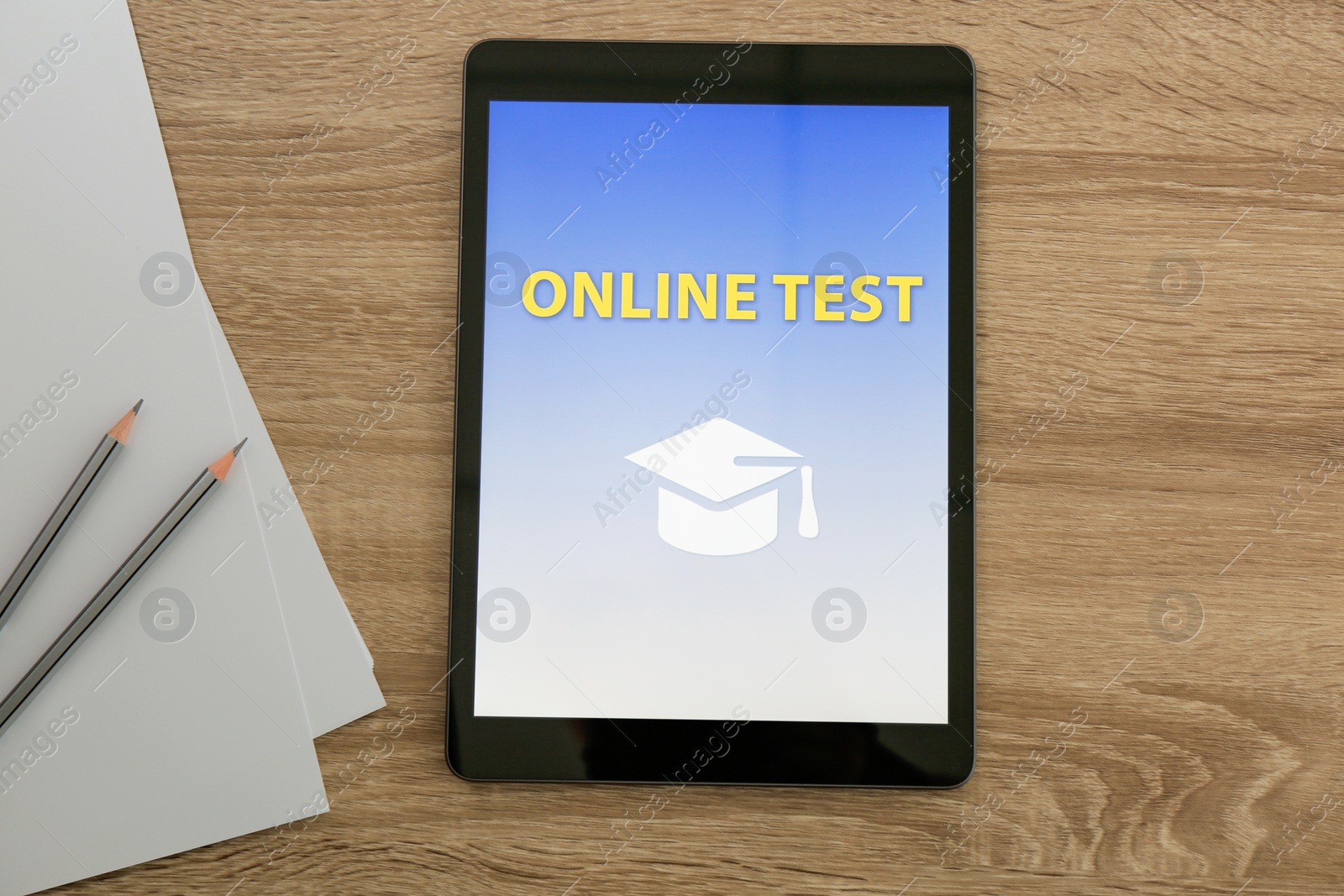 Photo of Modern tablet with online test, paper and pencils on wooden table, flat lay