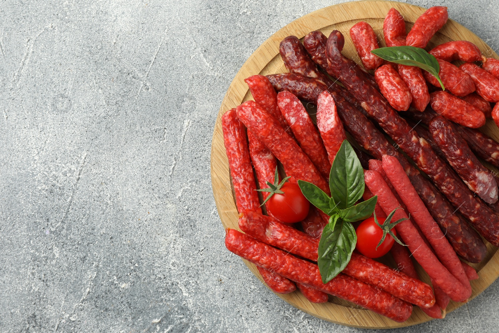Photo of Different thin dry smoked sausages, basil and tomatoes on light grey table, top view. Space for text