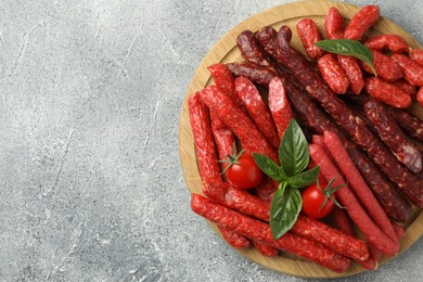 Different thin dry smoked sausages, basil and tomatoes on light grey table, top view. Space for text