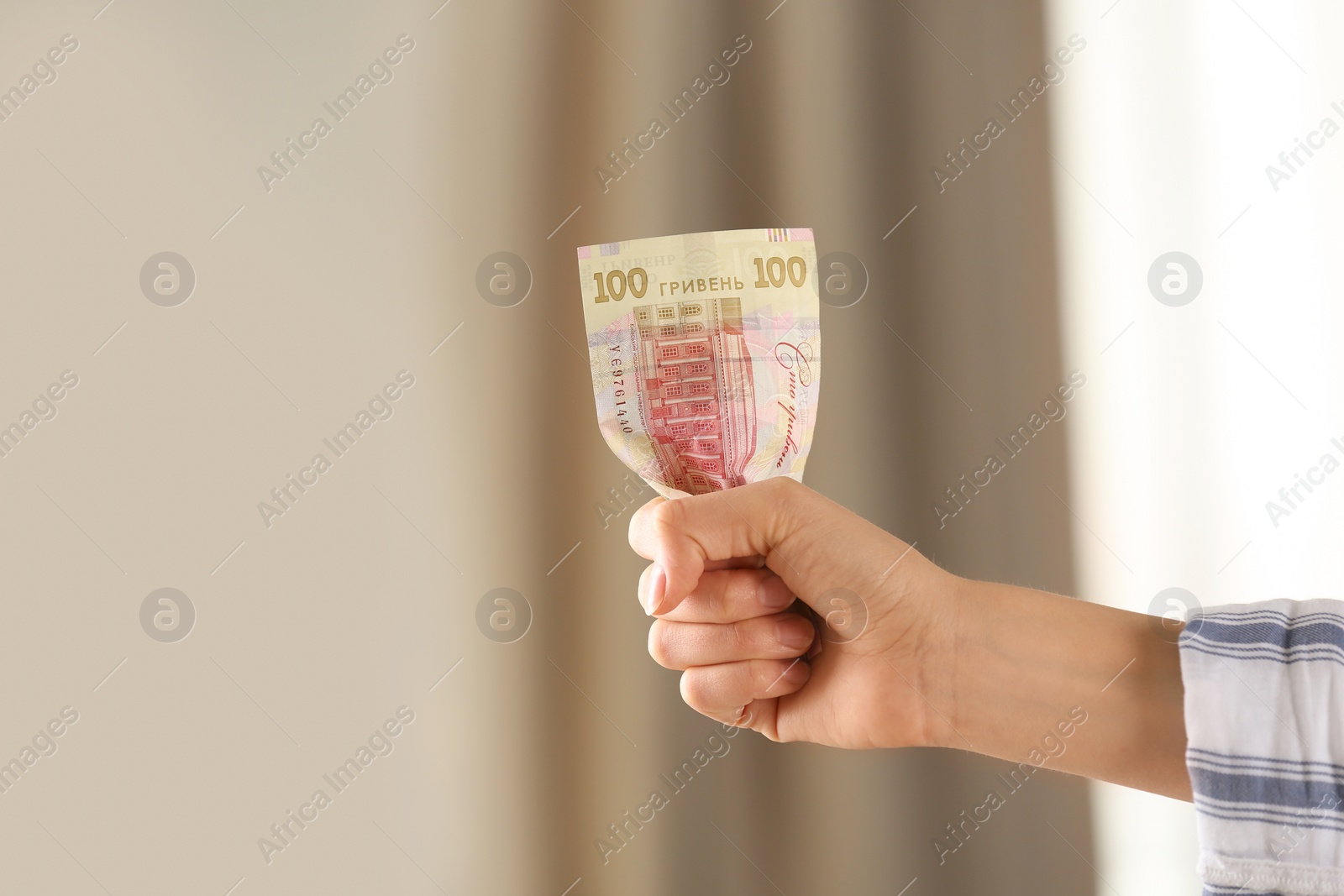 Photo of Woman holding 100 Ukrainian Hryvnias banknote against blurred background, closeup with space for text. International relationships