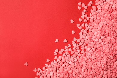 Bright heart shaped sprinkles on red background, flat lay. Space for text