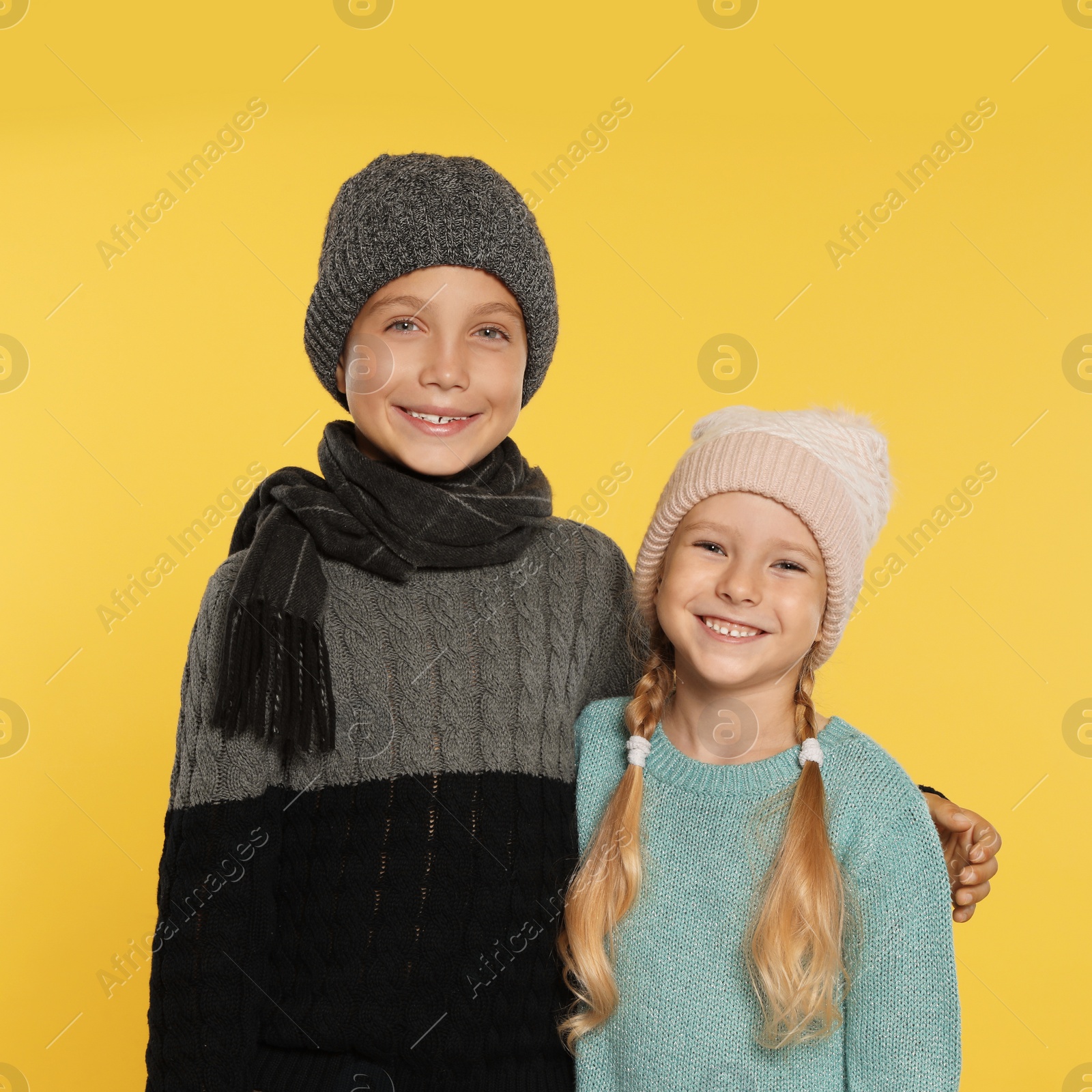 Photo of Cute little children in warm clothes on yellow background. Winter season