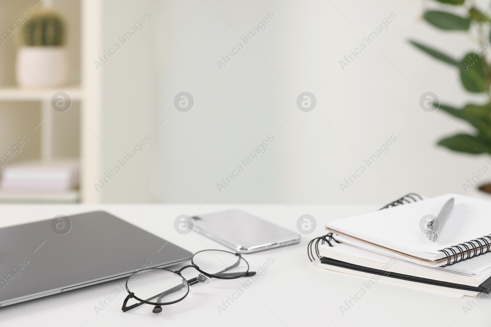 Photo of Home office. Laptop, glasses, notebooks, smartphone and pen on white desk indoors. Space for text