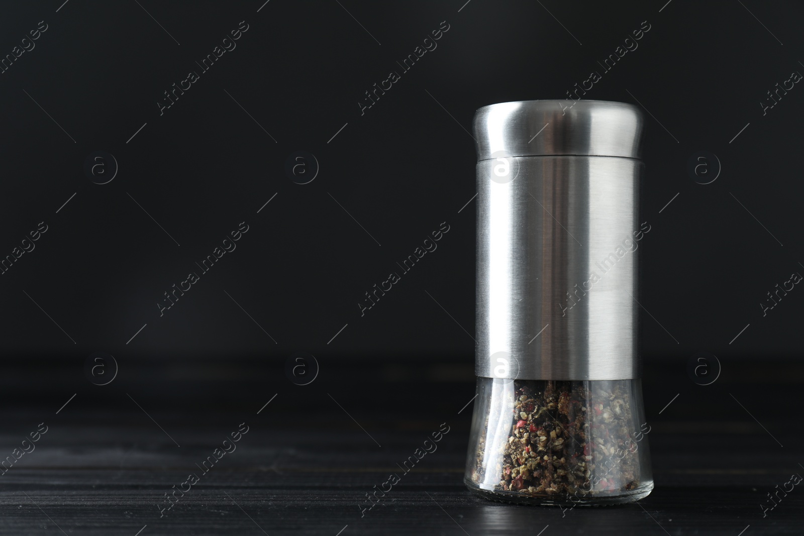 Photo of Pepper shaker on black wooden table, closeup. Space for text