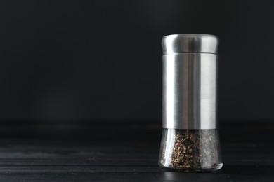 Photo of Pepper shaker on black wooden table, closeup. Space for text