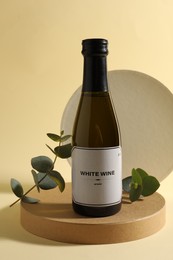 Photo of Bottle of delicious white wine and eucalyptus branches on beige background