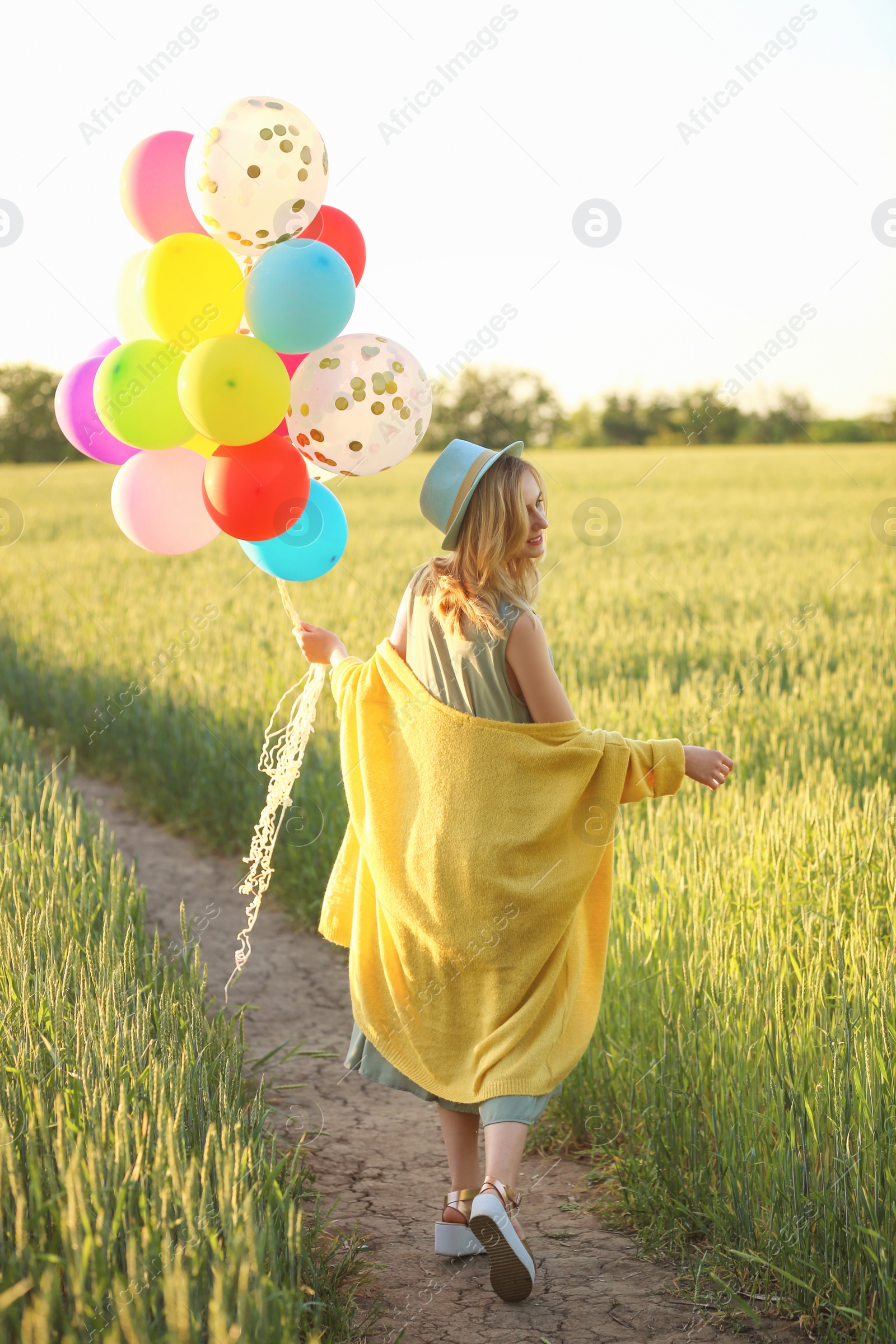 Photo of Young woman with colorful balloons in field on sunny day