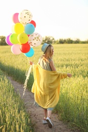 Young woman with colorful balloons in field on sunny day