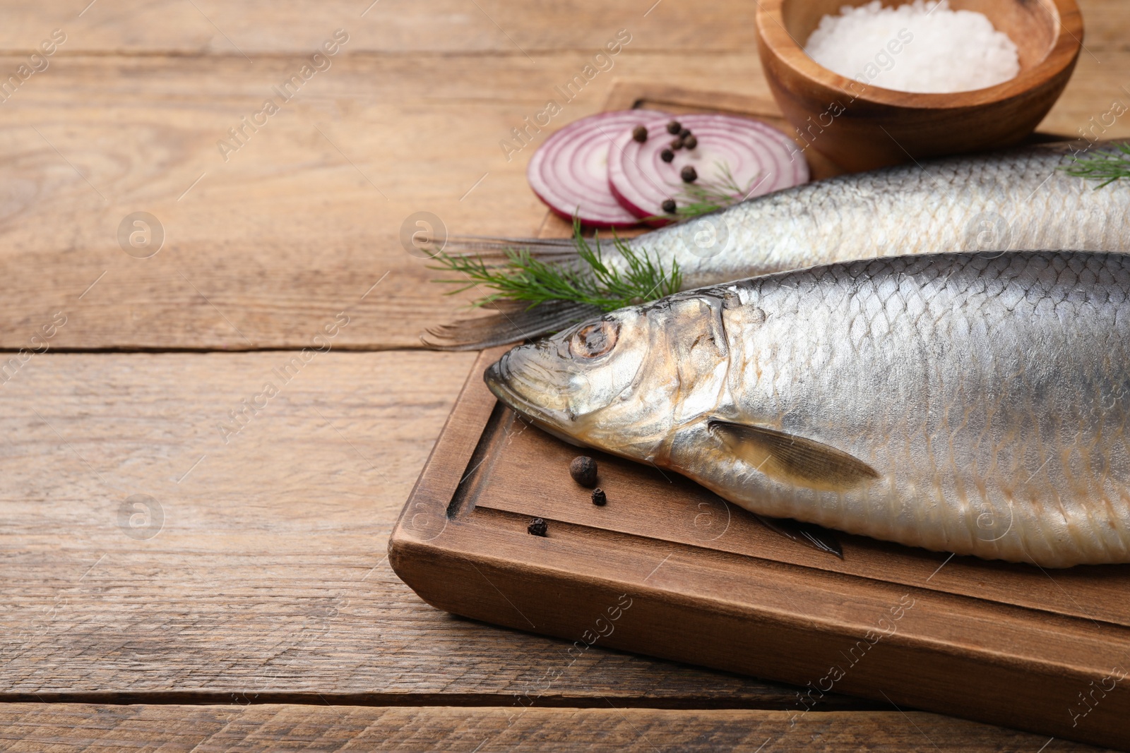 Photo of Board with delicious salted herrings, dill, onion and salt on wooden table. Space for text