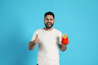 Photo of Young man with French fries on light blue background, space for text