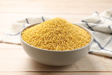 Photo of Millet groats in bowl on light wooden table, closeup