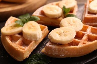 Photo of Tasty Belgian waffles with banana and mint on slate plate, closeup