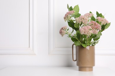 Photo of Stylish ceramic vase with beautiful flowers on table near white wall. Space for text