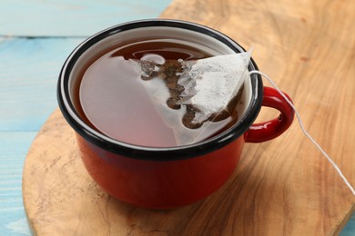 Photo of Tea bag in cup with hot drink on light blue wooden table, closeup