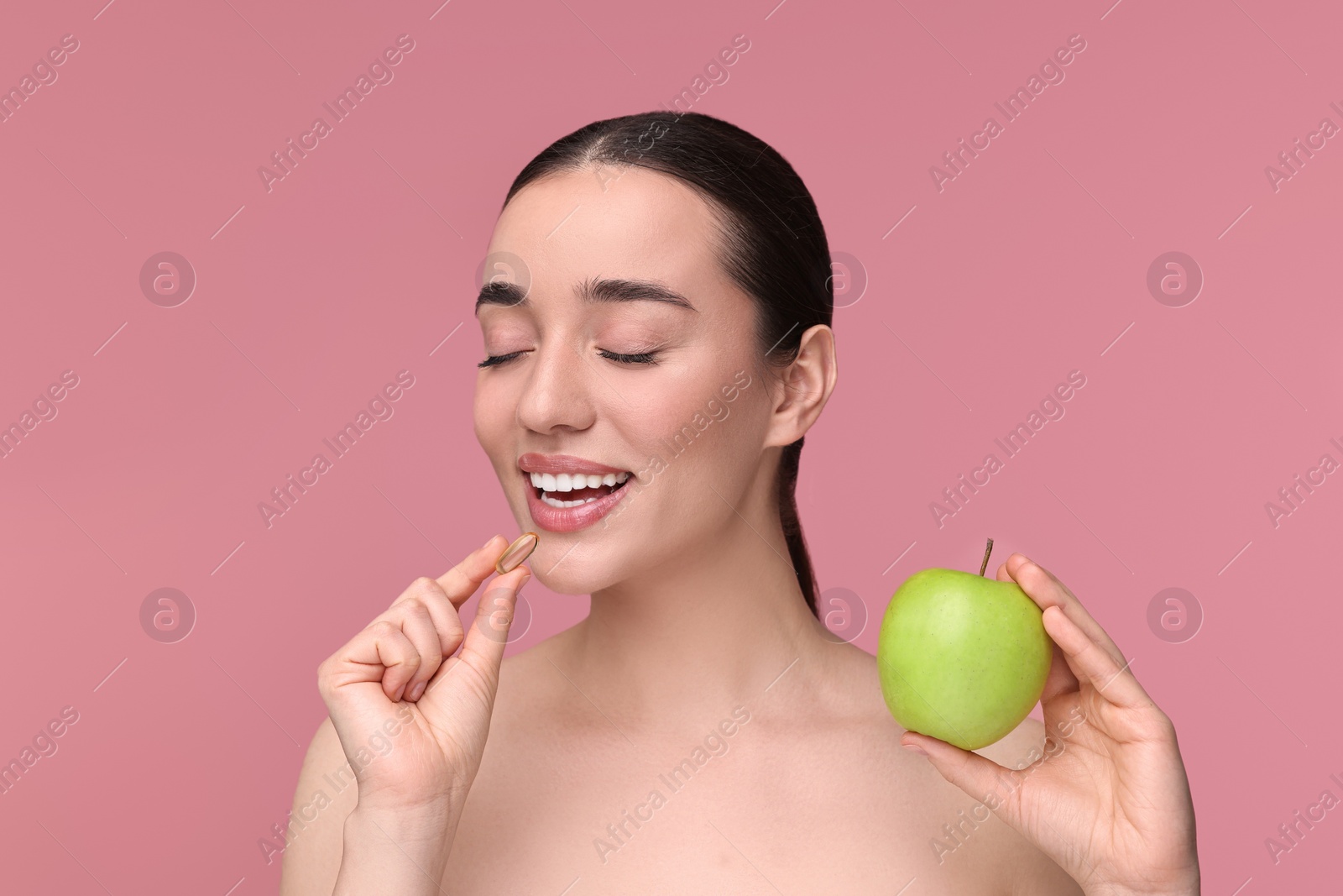Photo of Beautiful young woman with vitamin pill and apple on pink background