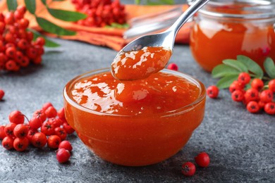 Delicious rowan jam in glass bowl and berries on grey table, closeup