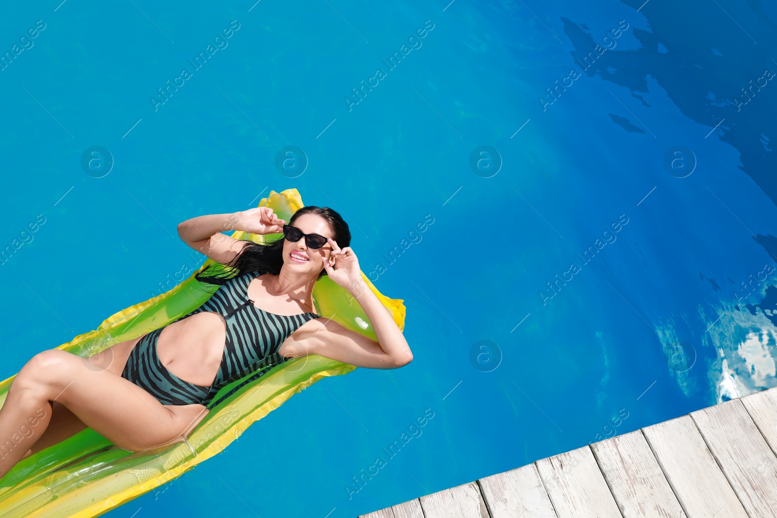 Photo of Beautiful young woman with inflatable mattress in swimming pool on sunny day, above view. Space for text