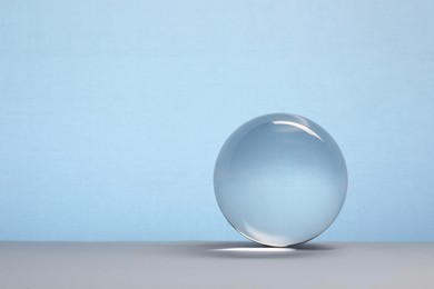 Photo of Transparent glass ball on table against light blue background. Space for text