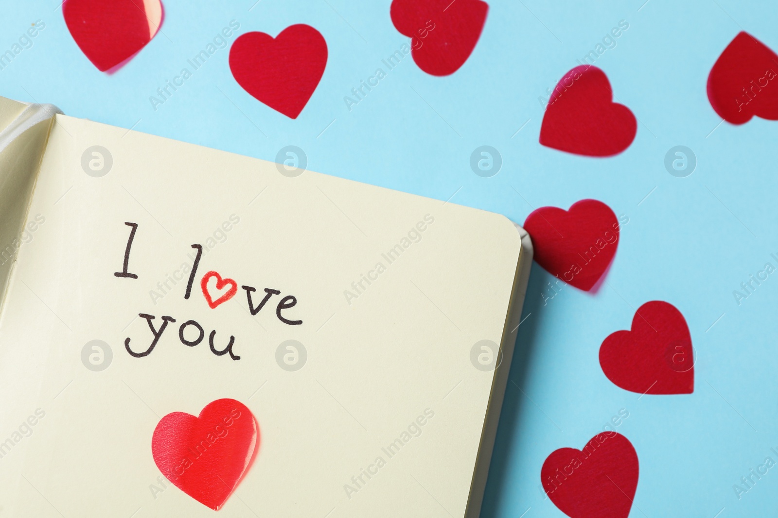 Photo of Notebook with text I Love You and hearts on light blue background, flat lay