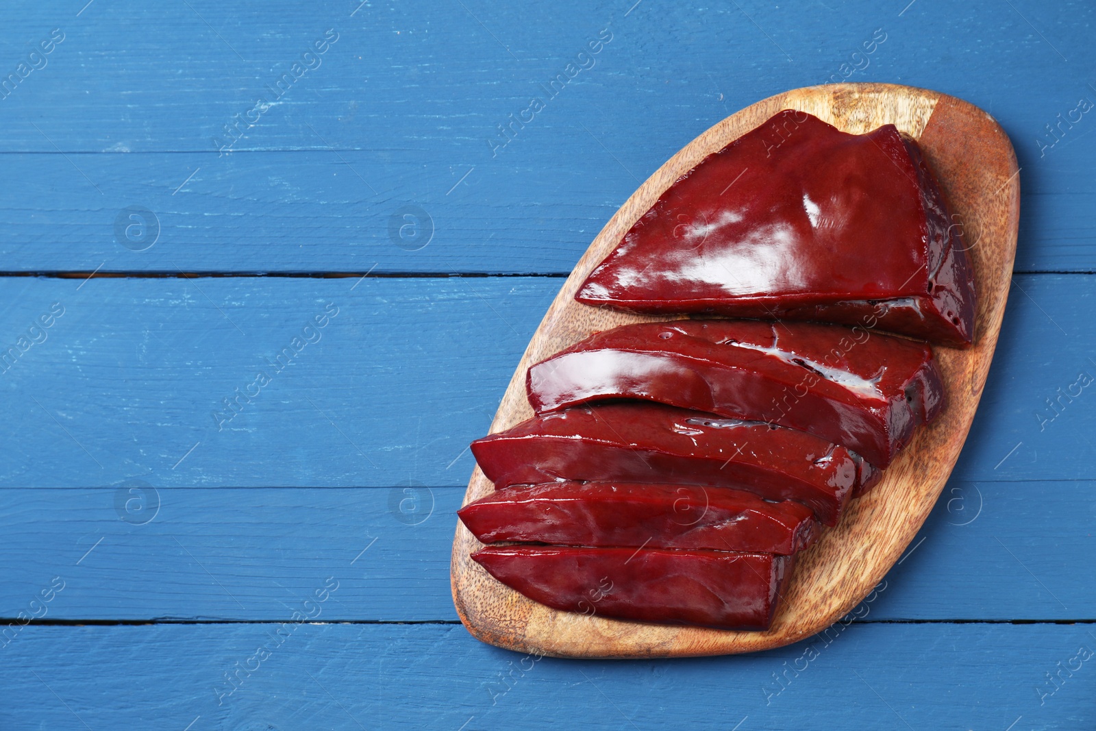 Photo of Cut raw beef liver on blue wooden table, top view. Space for text