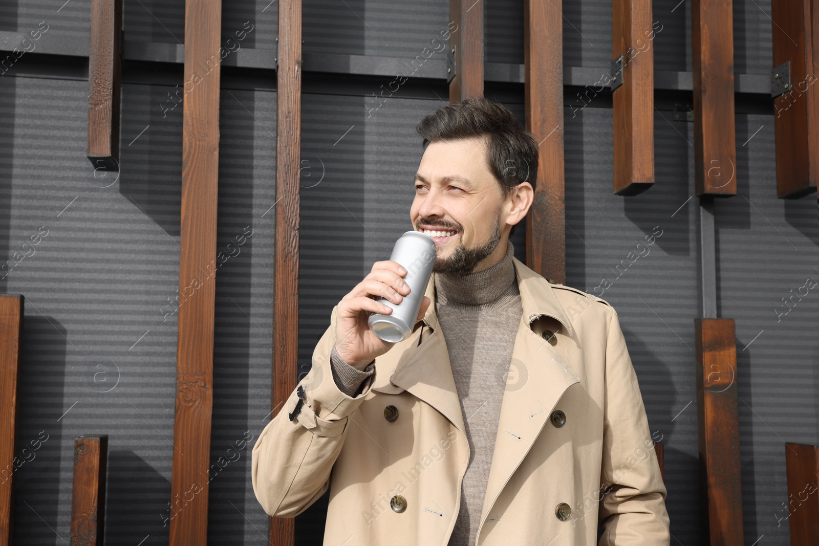 Photo of Happy man holding silver tin can with beverage outdoors