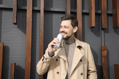 Photo of Happy man holding silver tin can with beverage outdoors