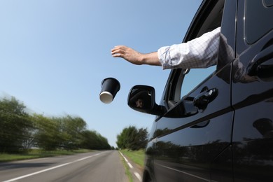 Photo of Driver throwing away paper coffee cup from car window. Garbage on road