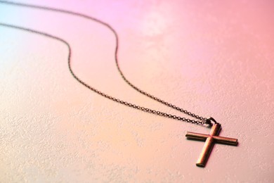 Photo of Cross with chain on textured table in color lights, closeup. Religion of Christianity