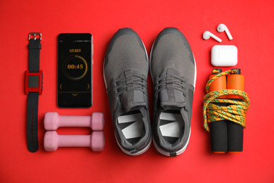 Smartphone with timer and fitness accessories on red background, flat lay