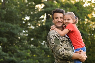 Photo of Father in military uniform holding his little daughter at green park
