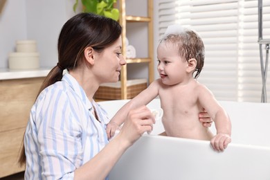 Mother bathing her cute little baby in tub at home