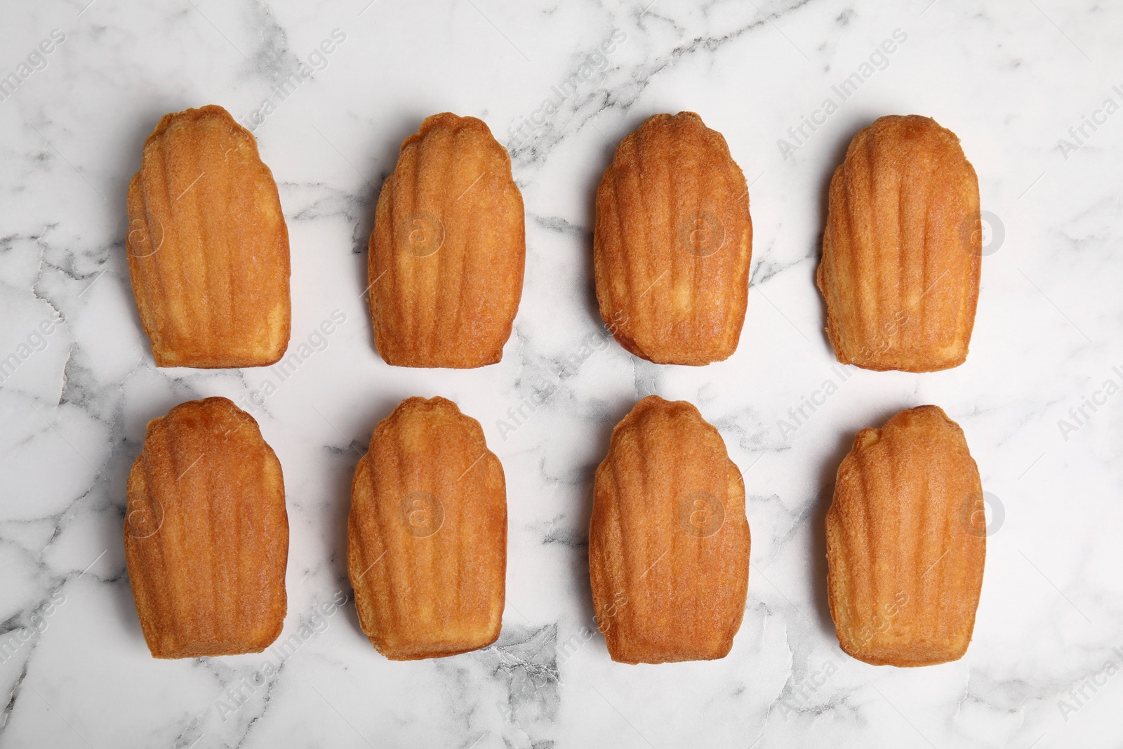 Photo of Delicious madeleine cakes on white marble table, flat lay