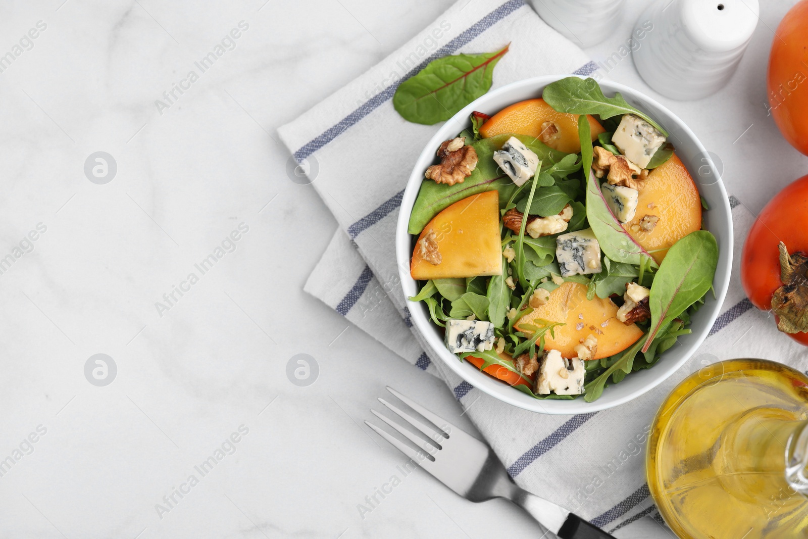 Photo of Tasty salad with persimmon, blue cheese and walnuts served on white marble table, flat lay. Space for text