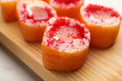 Photo of Delicious sushi rolls with salmon and tobiko on wooden board, closeup