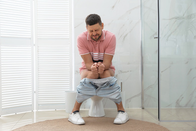 Man suffering from hemorrhoid on toilet bowl in rest room