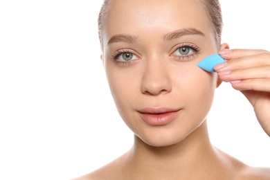 Photo of Young woman applying foundation on her face against white background