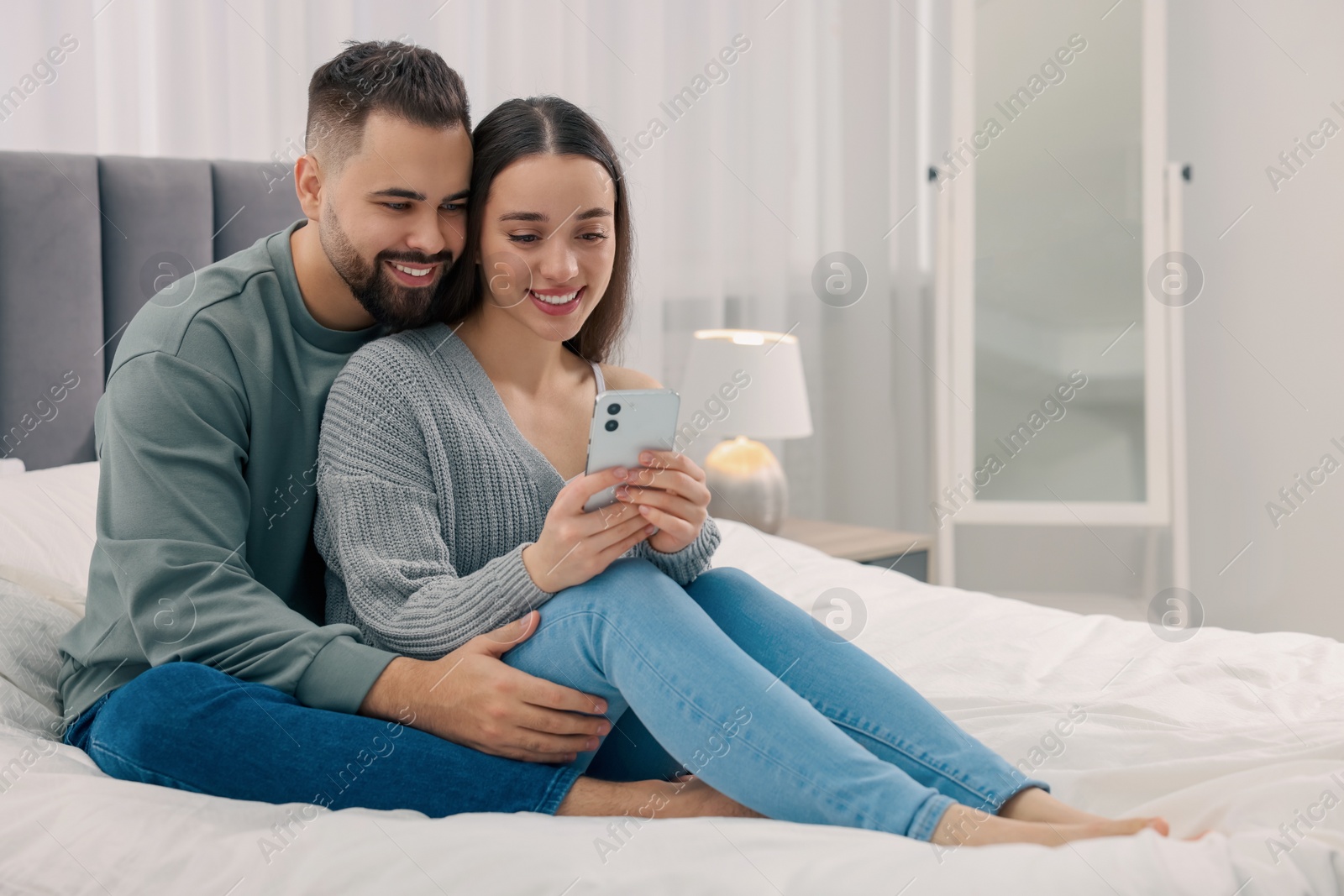 Photo of Happy young couple with smartphone in bedroom. Space for text