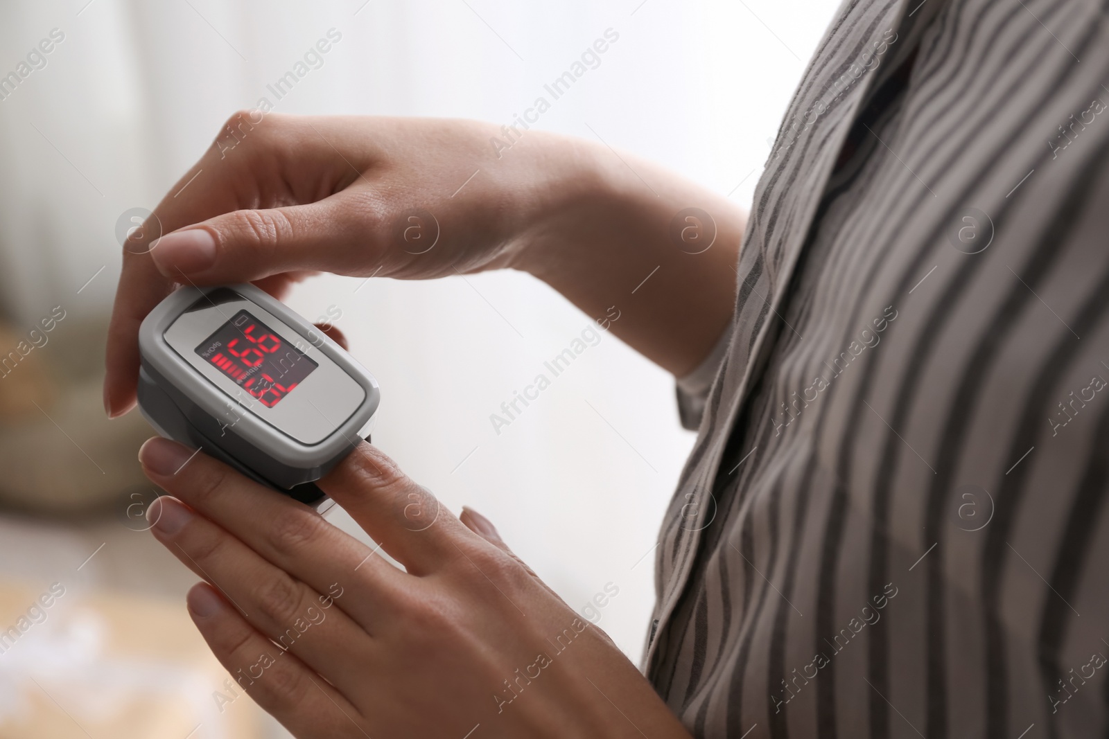 Photo of Woman measuring oxygen level with modern fingertip pulse oximeter indoors, closeup