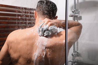 Photo of Man with mesh pouf taking shower at home, back view