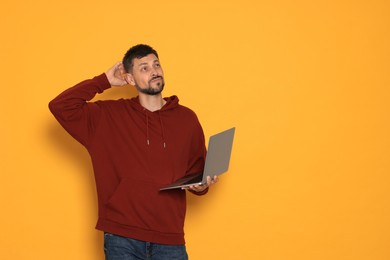Photo of Pensive man with laptop on orange background. Space for text
