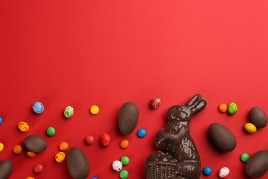 Photo of Flat lay composition with chocolate Easter bunny, eggs and candies on red background. Space for text