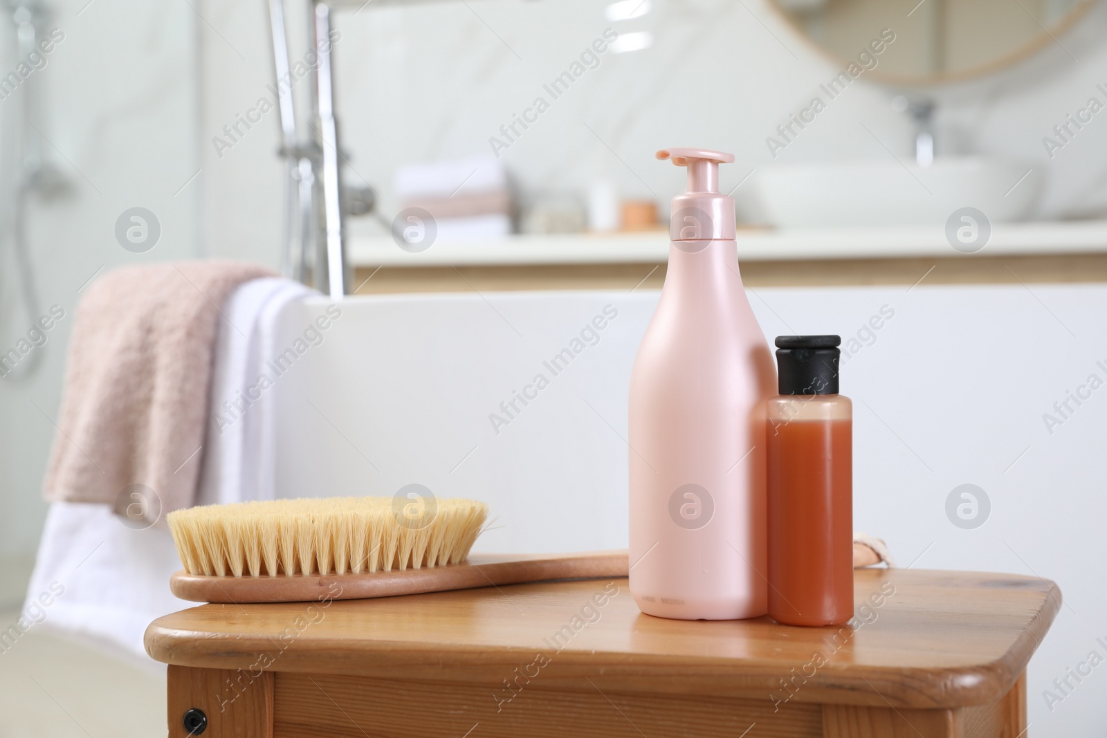 Photo of Bottles of shower gels and brush on wooden table near tub in bathroom, space for text