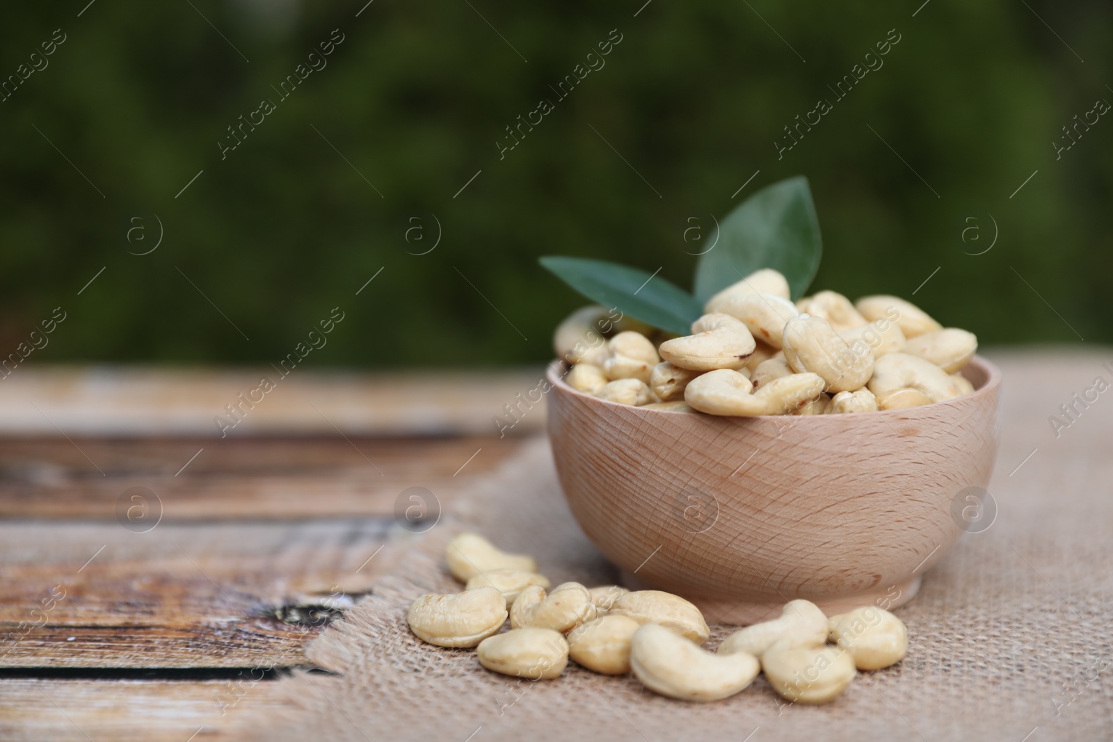 Photo of Tasty cashew nuts in bowl on wooden table outdoors, space for text