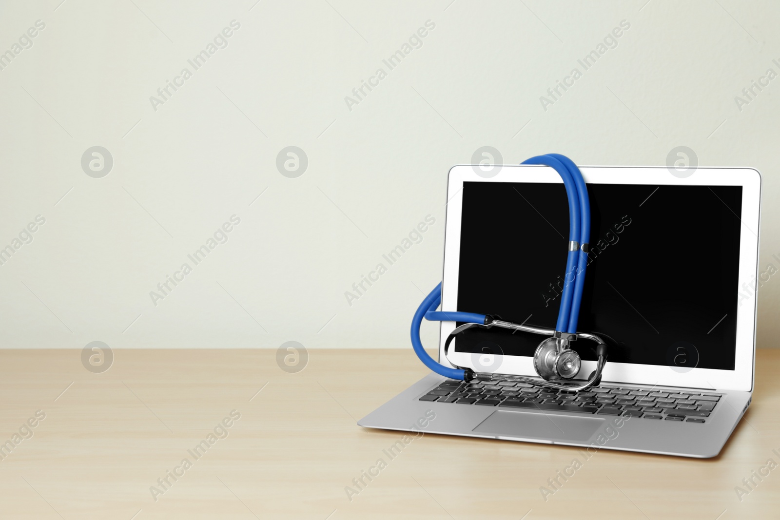 Photo of Laptop with blank screen and stethoscope on table against light background, space for text. Computer repair