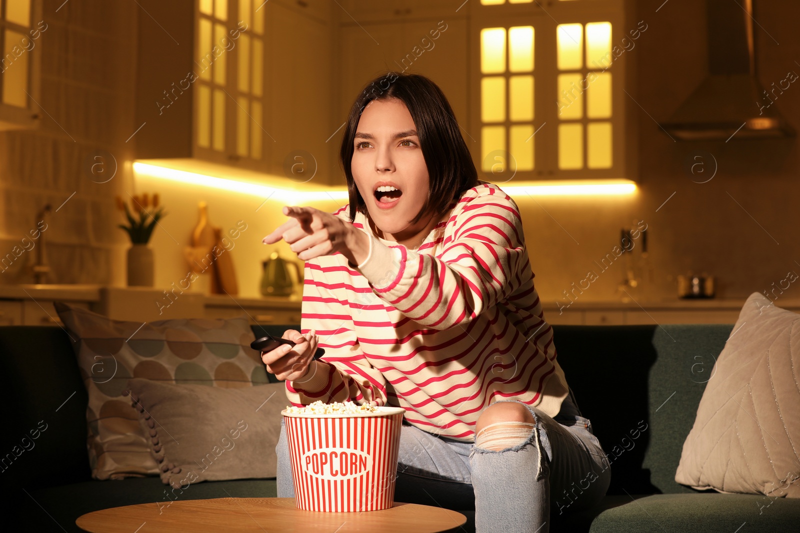 Photo of Surprised woman eating popcorn while watching TV on sofa at home